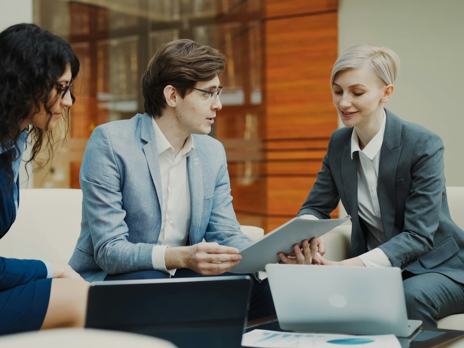 Trois professionnels en costume examinant des documents sur une tablette lors d’une réunion